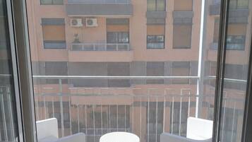 Een balkon met twee witte stoelen en een kleine ronde tafel, met uitzicht op een gebouw met meerdere balkons.