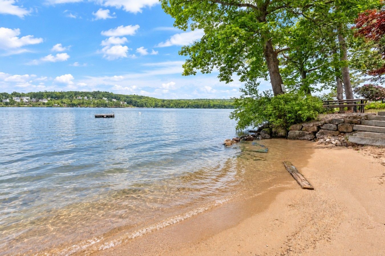 A clear lake with a sandy beach, a dock, and a stone staircase leading down to the water.