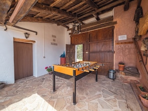 A rustic room with a foosball table, stone flooring, wooden beams, and a large wooden door.