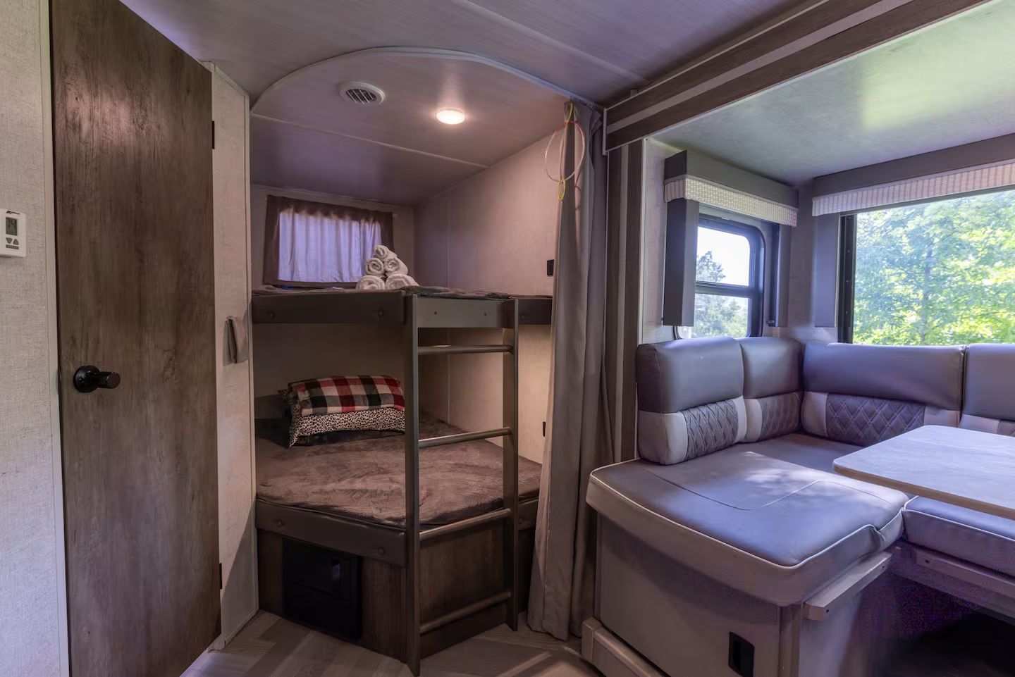 Un intérieur de camping-car compact comprenant un lit superposé, un coin salon avec des coussins et une petite table.