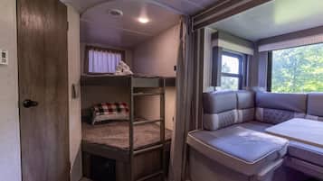 Un intérieur de camping-car compact comprenant un lit superposé, un coin salon avec des coussins et une petite table.