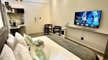 Un dormitorio con cama, televisor montado en la pared, escritorio pequeño y una silla.