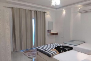 Una camera da letto con un letto, un comodino, una lampada a sospensione, una finestra con tende e un condizionatore d'aria a parete.