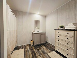 Une salle de bain avec un plancher en bois, un lavabo avec un miroir au-dessus et un meuble avec des tiroirs.