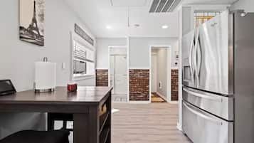 A modern kitchen with a stainless steel refrigerator, a dining table with a white napkin holder, and a brick accent wall.