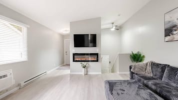 Un salon moderne avec une cheminée, un téléviseur à écran plat fixé au-dessus, et un canapé gris.