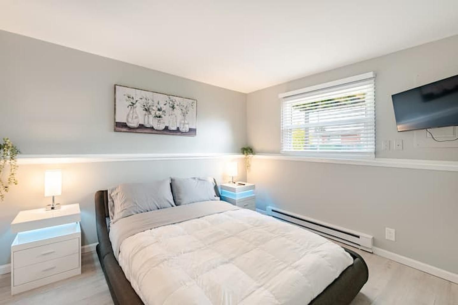 Une chambre à coucher avec un lit, des tables de chevet, une télévision et une fenêtre avec des stores.
