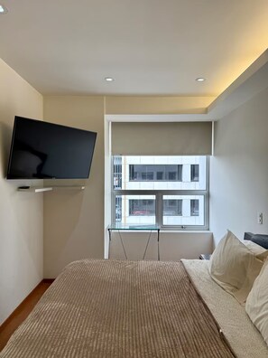 A modern bedroom with a flat-screen TV mounted on the wall, a large window with a view of a building, and a bed with a striped rug. - Insurgentes · Estacionamiento, gym y roof garden (Ciudad de México)
