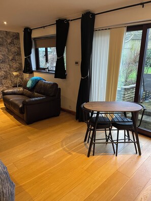 Ein stilvolles Wohnzimmer mit einer Ledersofa, einem runden Holztisch und schwarzen Vorhängen.