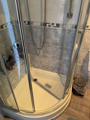 Eine gläserne Dusche mit Handbrause, Ablauforohr und Toilette mit Plastikbeutel.