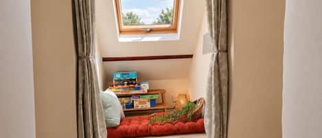 A room with a skylight, a shelf with boxes, a cushioned bench, and a small table with a lamp.