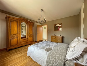 Un dormitorio con un armario grande, una cama con ropa de cama estampada, un tocador y un espejo en la pared.