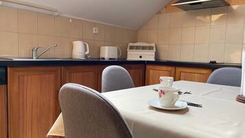 A kitchen with a dining table set for two, a kettle, a toaster, and a microwave.