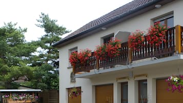 Un bâtiment à deux étages doté d’un balcon orné de fleurs rouges, d’une enseigne indiquant « LE LOUVETAS » et d’une clôture en bois.