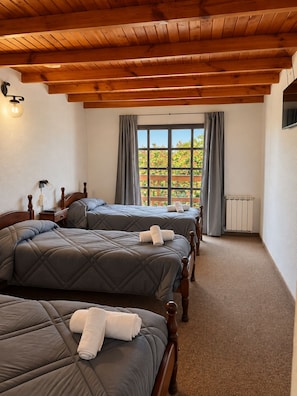 Una camera d'albergo con due letti, una finestra con tende, un termosifone e travi in legno al soffitto.