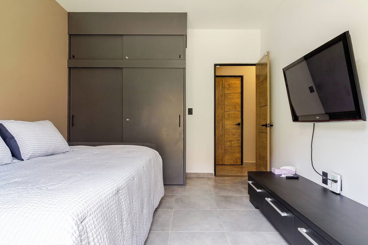 Quarto com cama, guarda-roupa, televisão e porta.