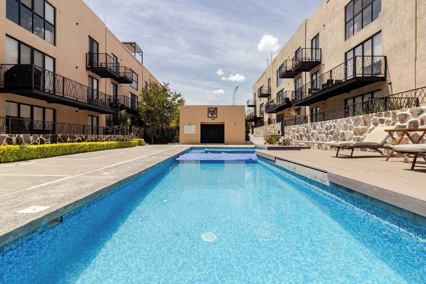 Uma piscina com uma parede de pedra de um lado e um edifício com varandas do outro.