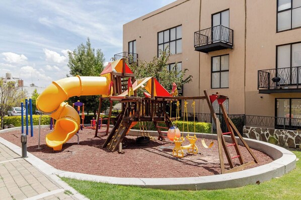 A playground with a slide and swings, surrounded by a landscaped area and a building with balconies. - Private Oasis in Querétaro (Santiago de Querétaro)
