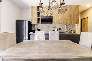 A modern kitchen with a dining table, chairs, a refrigerator, a microwave, and pendant lights. - Private Oasis in Querétaro (Santiago de Querétaro)
