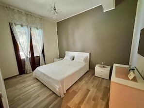 A bedroom with a bed, bedside tables, a nightstand, a chandelier, and a window with curtains. - Villa 'Perla Di Sicilia' with Private Pool, Wi-Fi and Air Conditioning (Campofelice di Roccella)