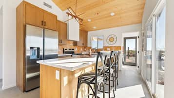 A modern kitchen with wooden cabinets, stainless steel appliances, and a bar area with stools.