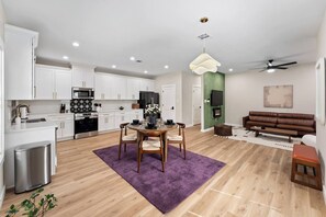 Una cocina moderna con armarios blancos, una zona de comedor con alfombra púrpura, un sofá de cuero marrón y una chimenea.
