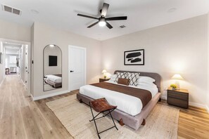 Un dormitorio moderno con una cama grande, lámparas de noche, ventilador de techo y un espejo.