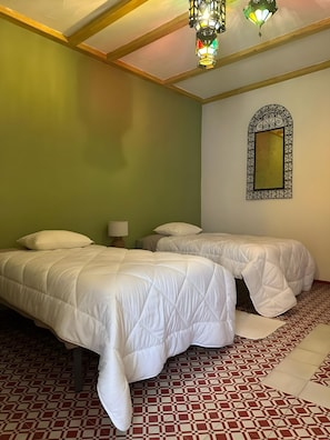 Ein Zimmer mit zwei Betten, einem gemusterten Boden und einem Zier-Spiegel.