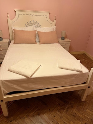 Una cama con cabecera blanca, dos almohadas y una toalla doblada sobre la cama.