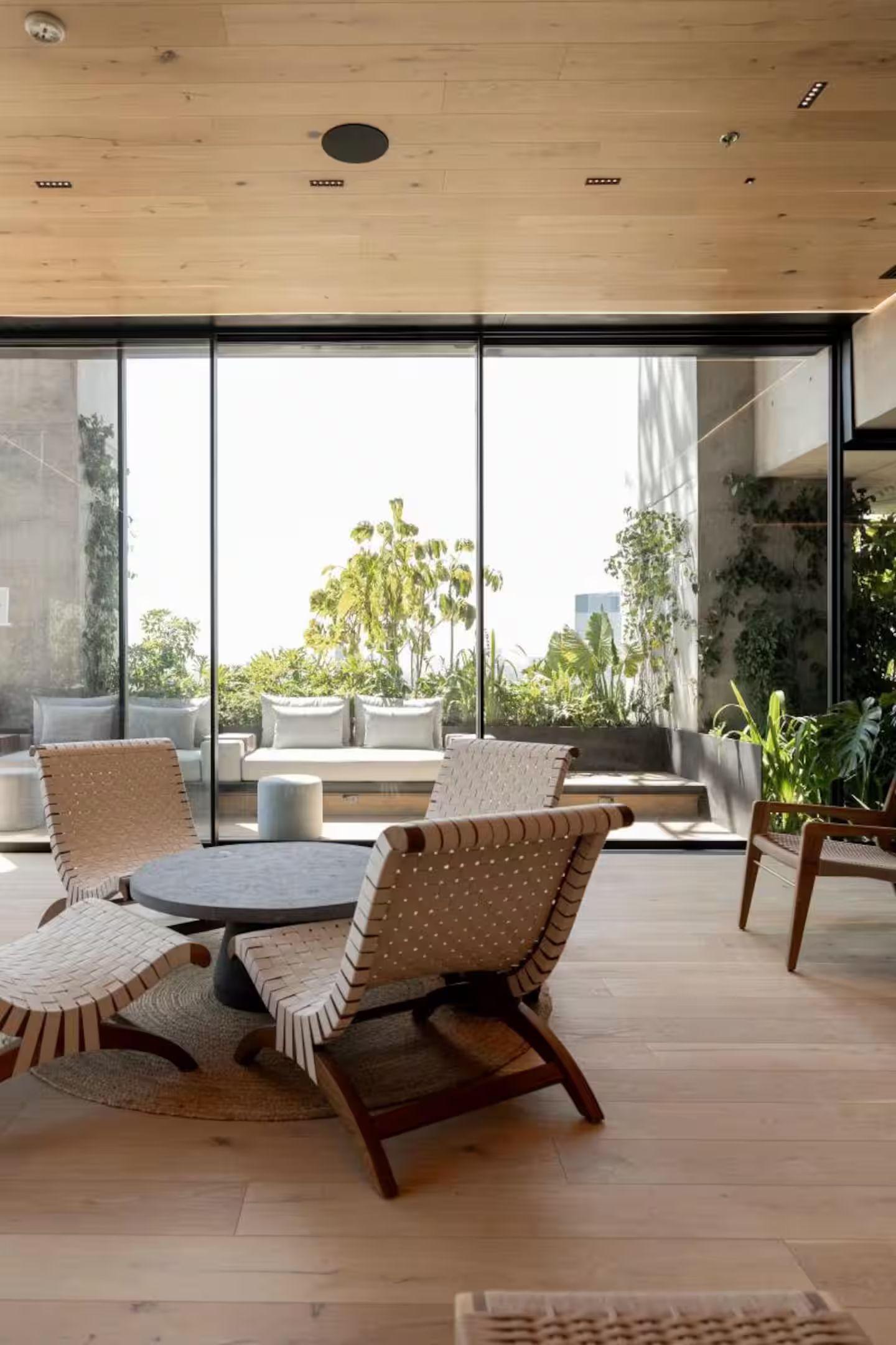 A modern outdoor seating area with a round table and chairs, large windows, and a view of greenery and buildings.
