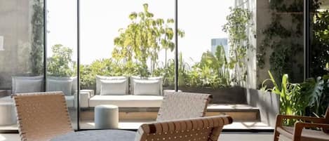 Un espace extérieur moderne, aménagé avec une table ronde et des chaises, de grandes fenêtres et une vue sur la verdure et les bâtiments.