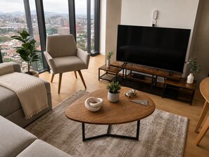 Una sala de estar moderna con un sofá, una mesa redonda de centro, un televisor y vistas a la ciudad.