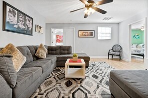 A living room with a sectional sofa, a coffee table, a patterned rug, a ceiling fan, and artwork on the walls. - Just a Dream Away: 9-Bedroom Pool and Spa Home with Game Room (ChampionsGate)
