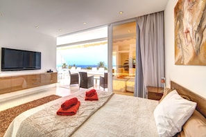 Een hotelkamer met een bed, een televisie, een balkon met uitzicht op zee en een zithoek.