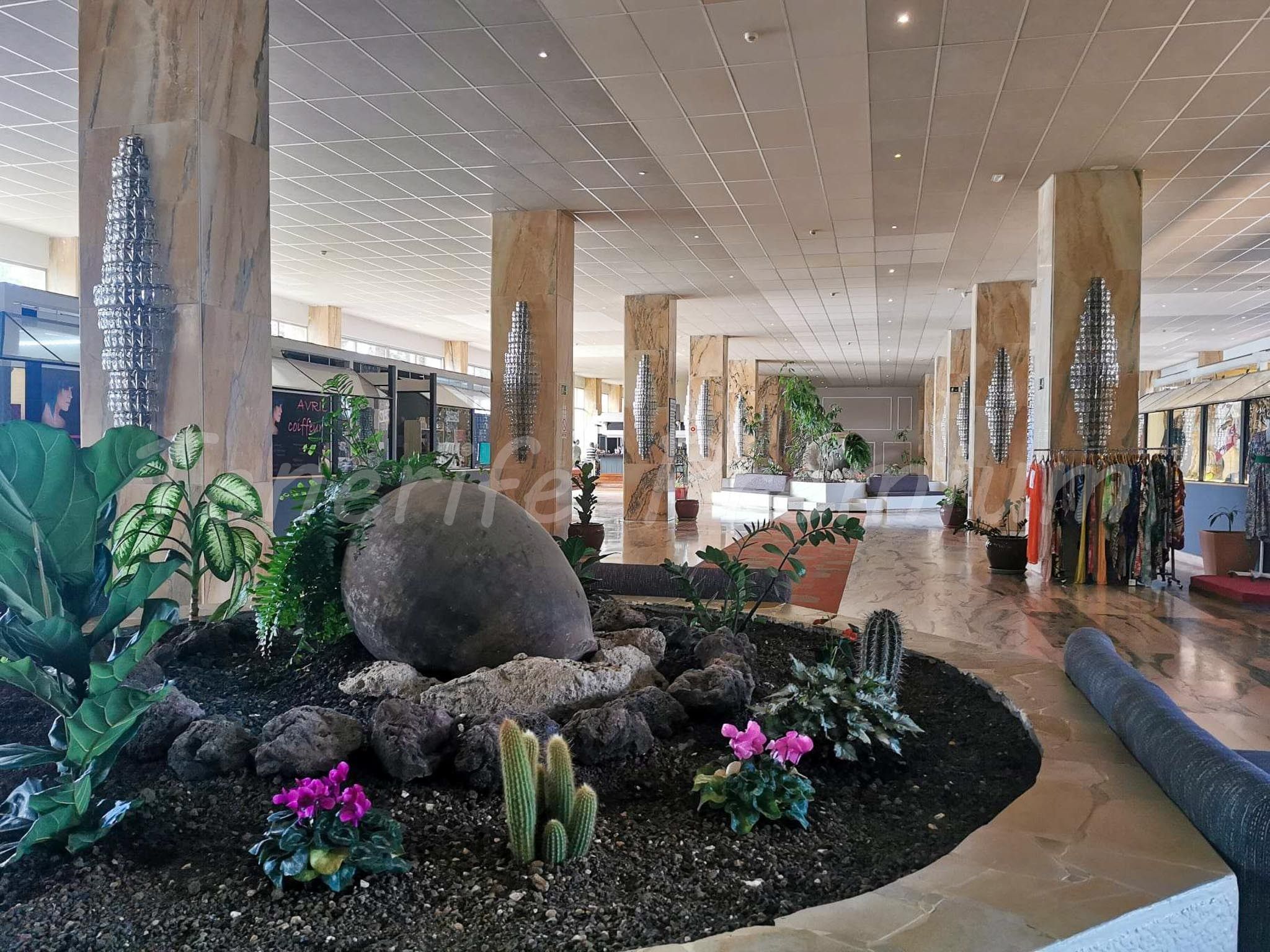 Ruime binnenruimte met een centrale rotstuin, omringd door grote pilaren en diverse planten.