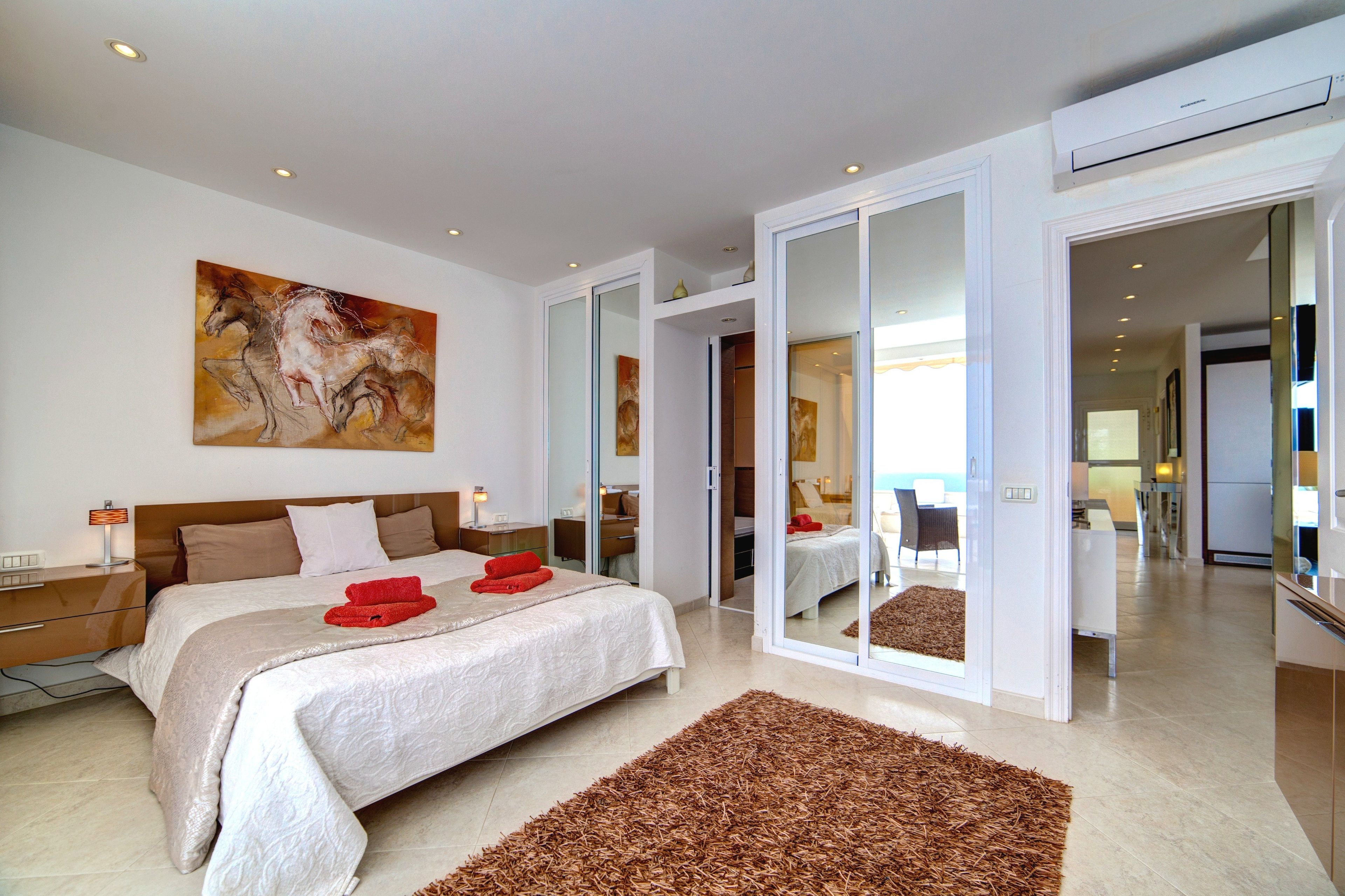 A modern hotel room with a large bed, a painting, and a sliding glass door leading to a balcony.