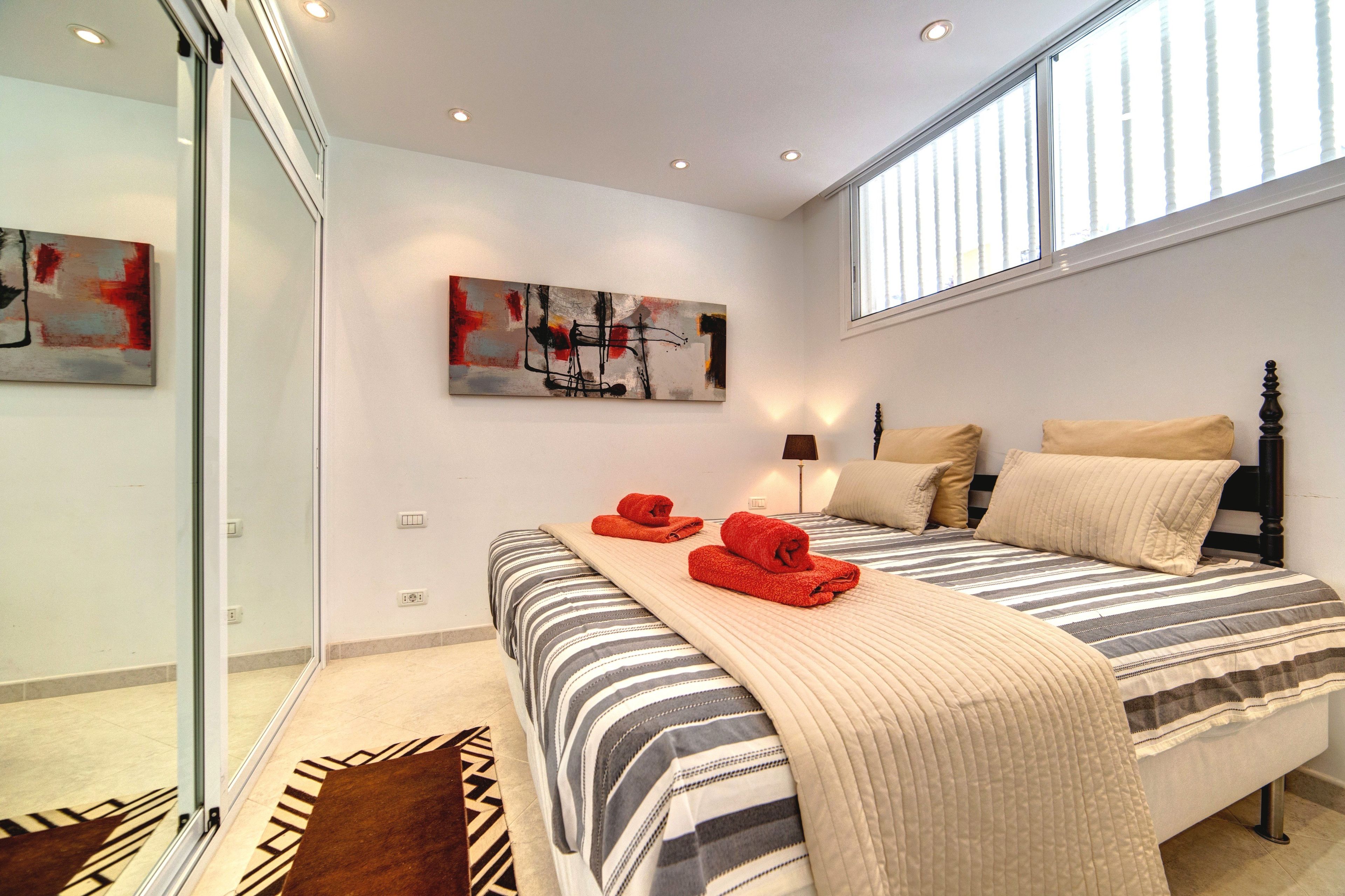 Une chambre à coucher avec un lit, des oreillers, une couverture, un tableau et une fenêtre.
