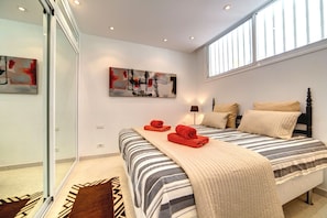 Een slaapkamer met een bed, kussens, een dekbed, een schilderij en een raam.