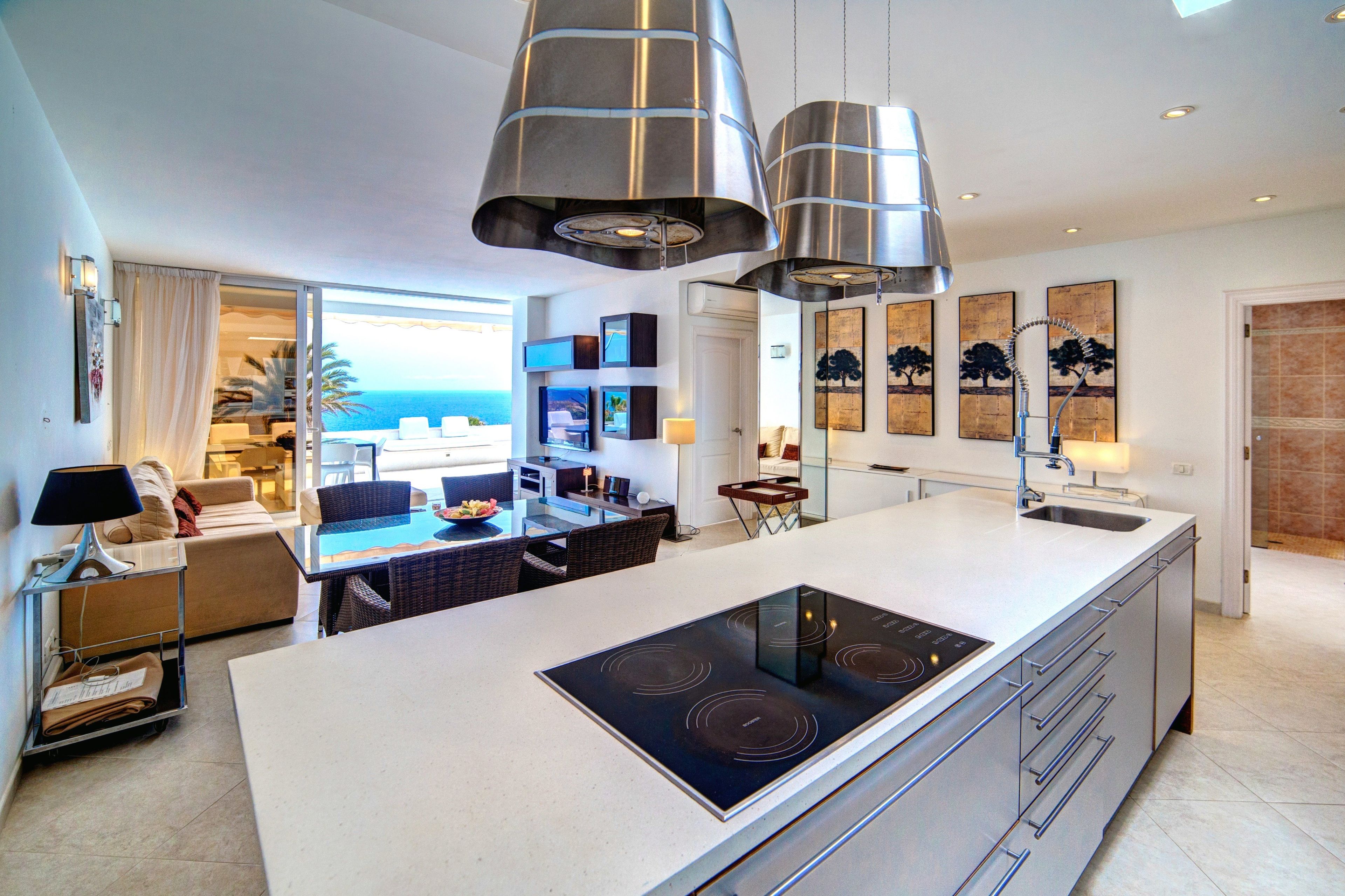 Een moderne keuken met een centraal eiland, verlichting boven en uitzicht op de woonkamer.