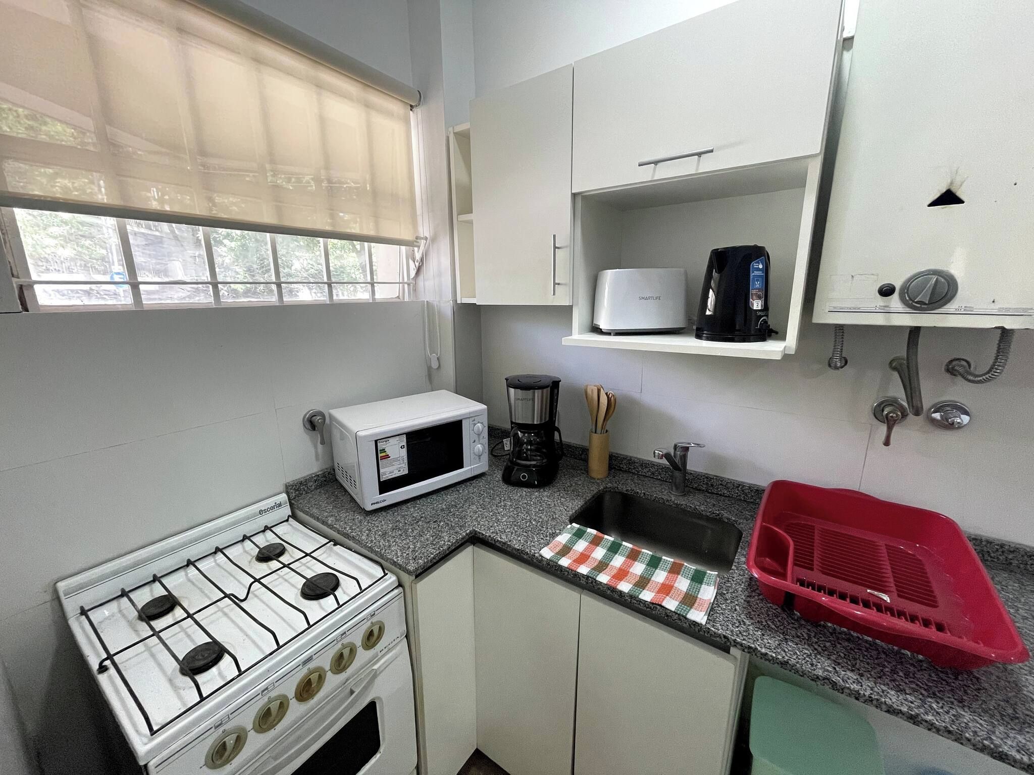Una cocina compacta con estufa a gas, microondas, cafetera y pileta.