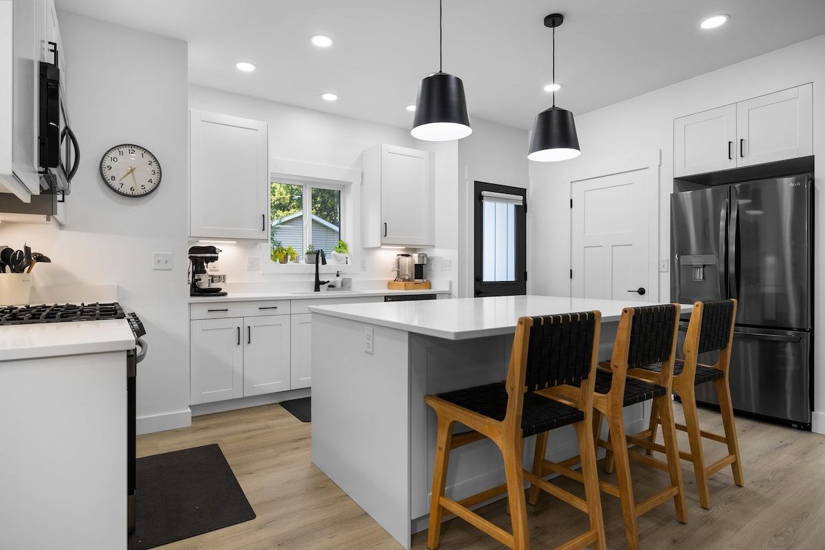 A modern kitchen with white cabinetry, a stainless steel refrigerator, and a central island with bar stools.