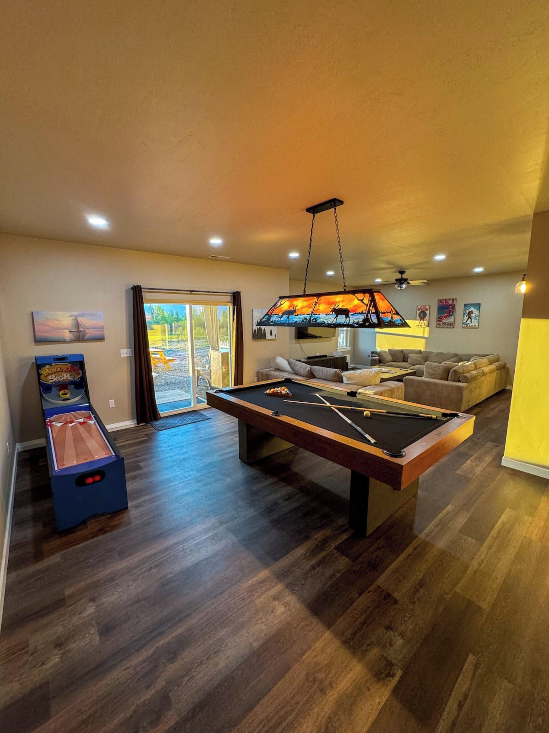 Un grand espace de vie comprenant une table de billard, un ensemble de canapés et une table de billard surmontée d’un luminaire décoratif.