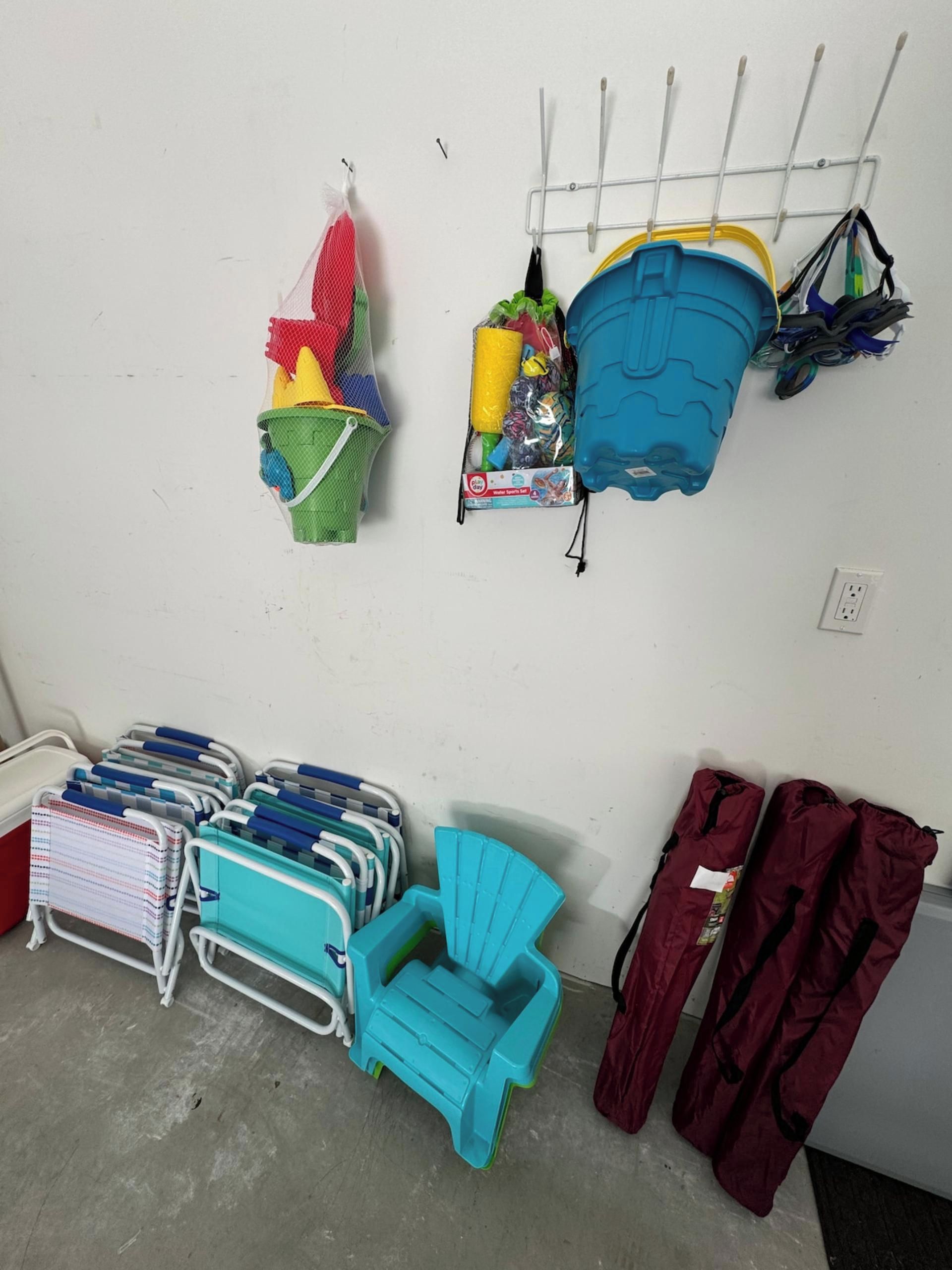 A room with a white wall, a metal rack with various items, a blue chair, a red bag, and a white floor.