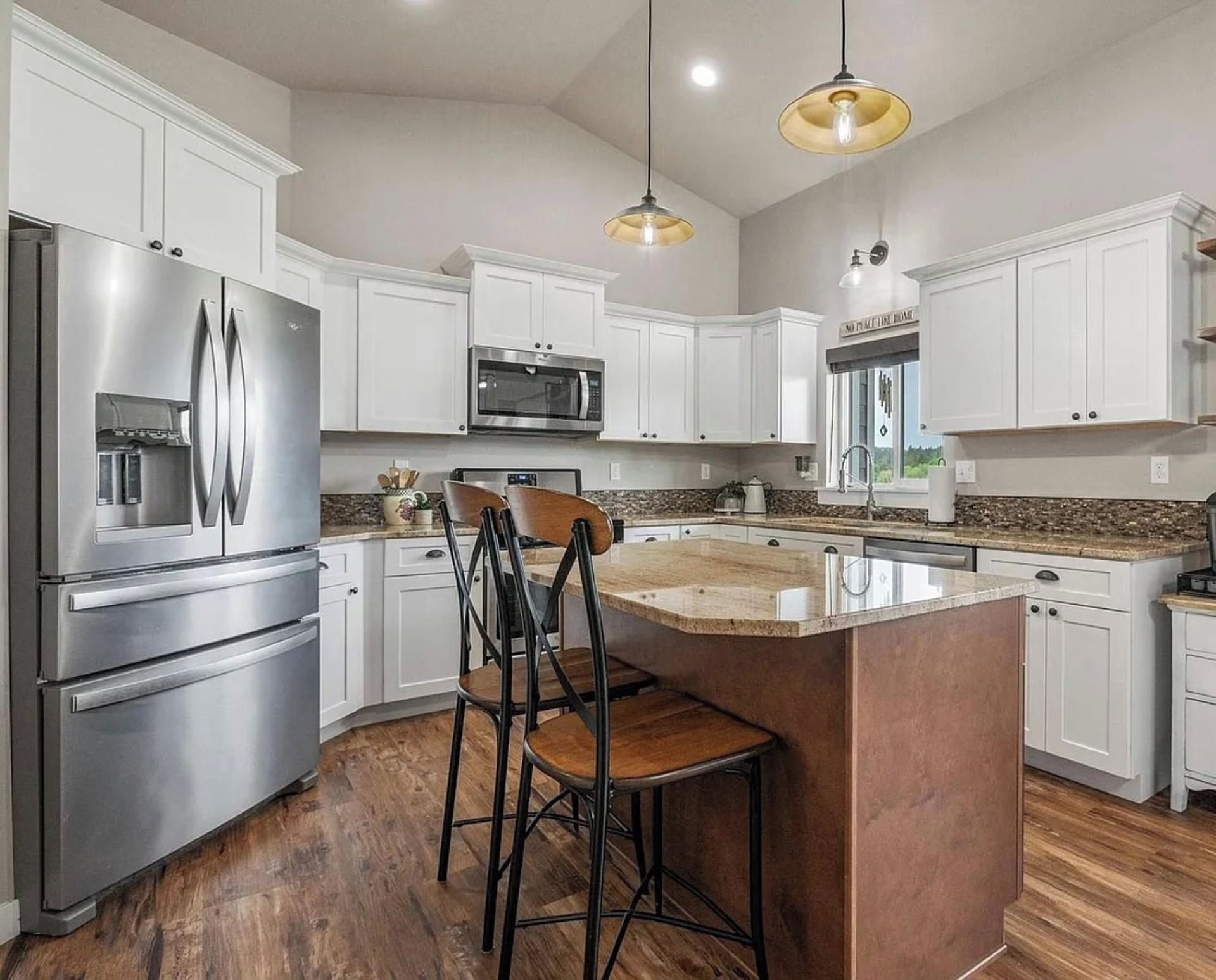 A modern kitchen with stainless steel appliances, white cabinetry, and a central island with bar stools.