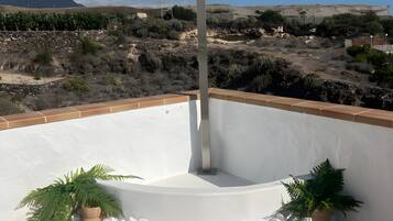 Terraza en la azotea con pared blanca, un poste metálico y plantas en macetas.