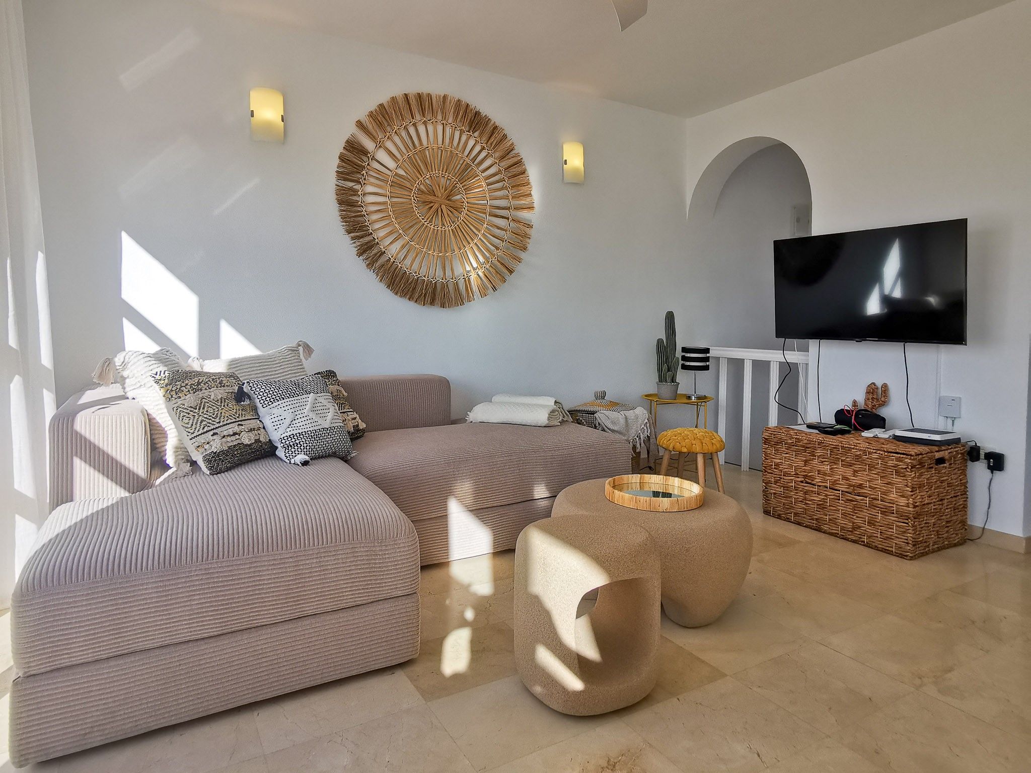 Een moderne woonkamer met een hoekbank, een ronde salontafel en een flatscreen televisie aan de muur.