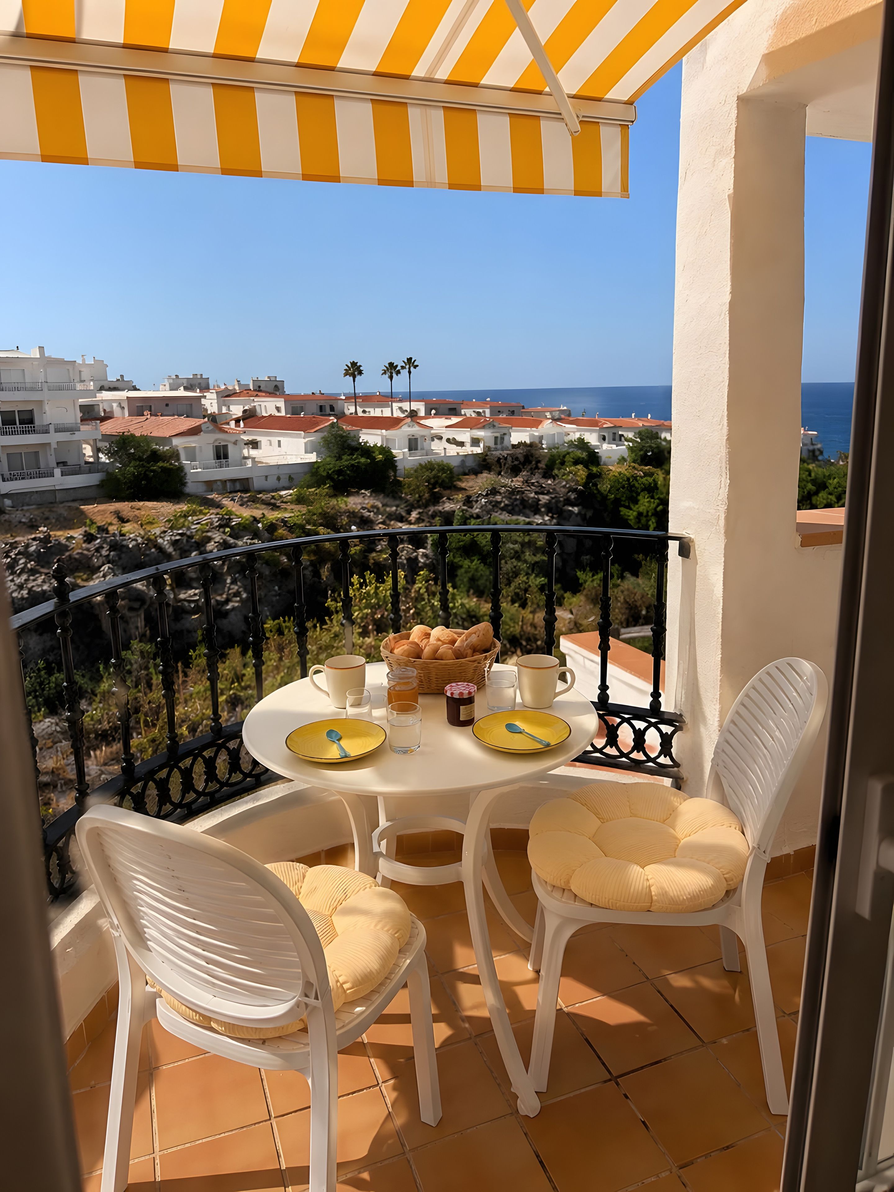 Een balkon met een tafel gedekt voor twee personen, met uitzicht op een kustplaats.