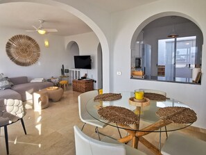 Een moderne woonkamer met een glazen eettafel, witte banken en een flatscreen televisie.
