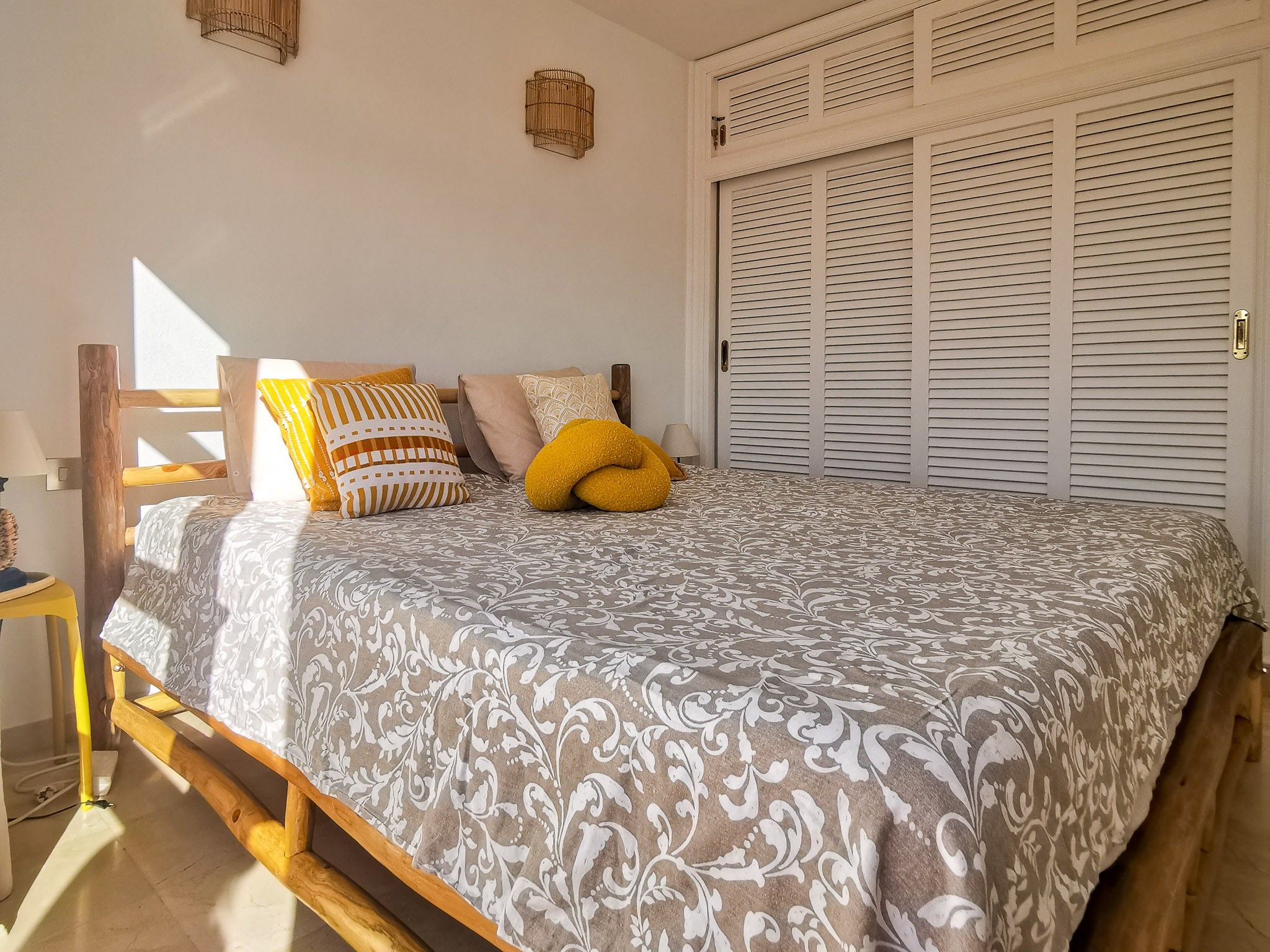 Een slaapkamer met een bed, kussens, een nachtkastje en een kledingkast.