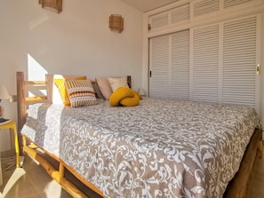 Een slaapkamer met een bed, kussens, een nachtkastje en een kledingkast.